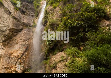 Une chute d'eau descendant en cascade une falaise rocheuse entourée d'une végétation luxuriante en saison estivale Banque D'Images
