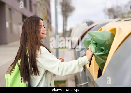 Jeune femme jetant des ordures dans le bac de recyclage sur la rue de la ville Banque D'Images