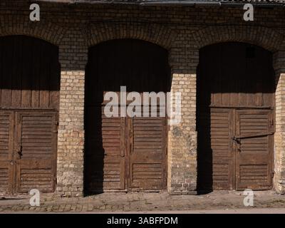 Vieux bâtiment en briques avec portes en bois vieilli à la lumière du soleil chaude. Banque D'Images