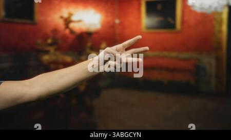 Main d'homme montrant trois doigts à l'intérieur dans une salle de musée avec des murs rouges et un décor classique. Banque D'Images
