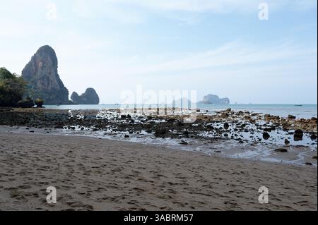 La marée basse sur la plage de Tonsai révèle des textures rocheuses et des falaises calcaires sous un ciel matinal doux Banque D'Images