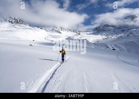 Randonneur de ski montant à travers un paysage de montagne pittoresque enneigé avec vue sur les sommets, ascension jusqu'à la cabane de montagne Chamanna es-cha, Bue Banque D'Images