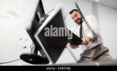 Заголовок : un homme d'affaires agressif perd son sang-froid dans un accès de rage. Un employé de bureau en colère brise un écran d'ordinateur avec son clavier. Banque D'Images