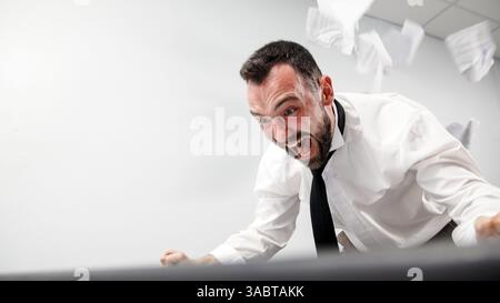 Заголовок : un homme d'affaires agressif perd son sang-froid dans un accès de rage. Un employé de bureau en colère brise un écran d'ordinateur avec son clavier. Banque D'Images