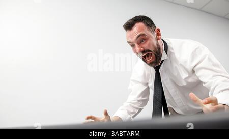 Заголовок : un homme d'affaires agressif perd son sang-froid dans un accès de rage. Un employé de bureau en colère brise un écran d'ordinateur avec son clavier. Banque D'Images