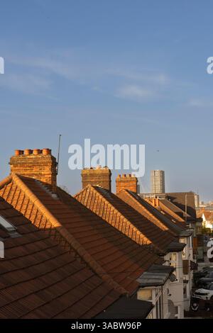 Maisons mitoyennes avec toits en terre cuite à Londres, probablement près d'un nouveau bâtiment de grande hauteur en construction. La lumière du soleil met en valeur les toits. Banque D'Images