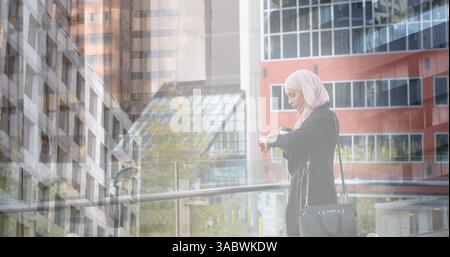 Image d'une femme asiatique en hijab utilisant smartwatch au-dessus du paysage urbain Banque D'Images