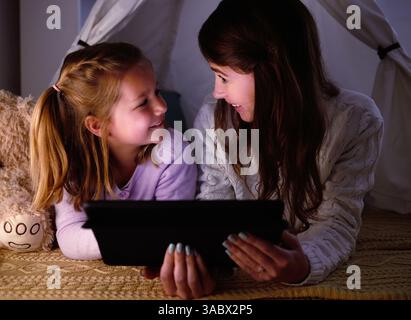 Tablette, tente et mère avec enfant pour lier à la maison en jouant à des jeux éducatifs ou des activités en ligne. Détendez-vous, couverture fort et maman avec la montre fille enfant Banque D'Images