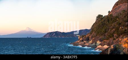 Un paysage panoramique captivant capturant l'emblématique Mont Fuji au coucher du soleil comme vu de l'autre côté de la baie de Suruga depuis la rive de Kumoni sur le pittoresque Izu du Japon. Banque D'Images