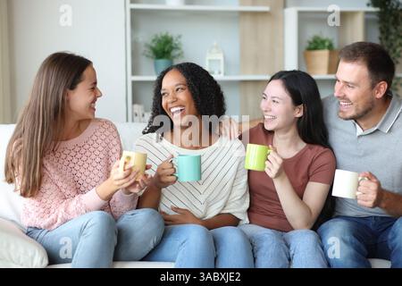 Heureux groupe d'amis parlant et buvant du café assis sur un canapé à la maison Banque D'Images