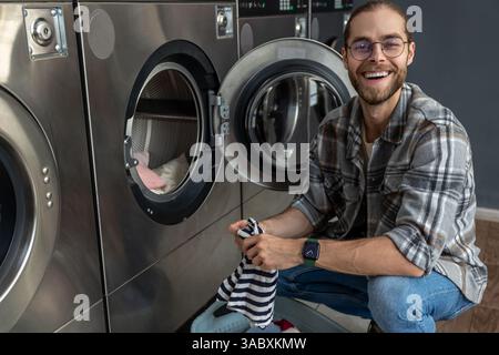 Homme utilisant une machine à laver à pièces qualifiée dans la salle publique pour laver ses chiffons Banque D'Images