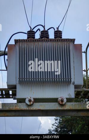 Une grande centrale électrique avec trois hauts poteaux et une grande boîte blanche sur le dessus. La boîte est entourée de nombreux fils et est entourée d'un fram en métal rouillé Banque D'Images