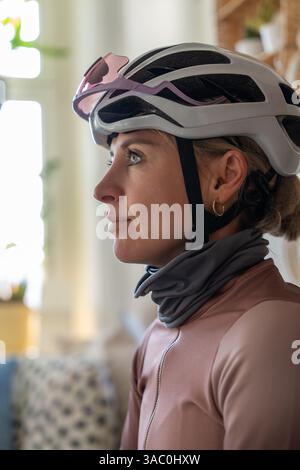Portrait en gros plan dans le profil de jolie femme cycliste. Jolie femme cycliste en casque, lunettes de soleil à la maison avant l'entraînement. Portrait sportif. Banque D'Images