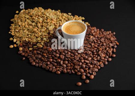 Une tasse blanche remplie de café est entourée de grains de café torréfiés et non torréfiés. Parfait pour les cafés ou les médias sur le thème du café. Banque D'Images