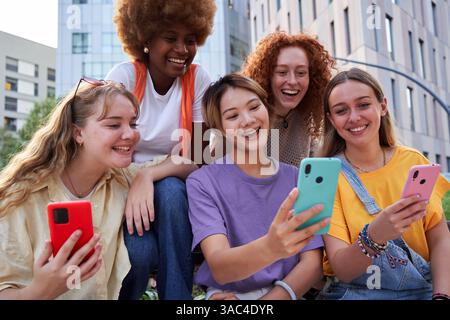 Groupe multiracial de femmes joyeuses se réunissant en plein air dans la ville, en utilisant des smartphones. Banque D'Images
