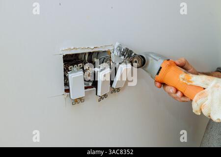 Électricien travaille sur le remplacement des interrupteurs muraux obsolètes tout en rénovant l'intérieur de la maison à l'aide d'outils multi-électriques Banque D'Images