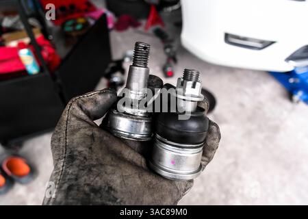 Comparaison des joints à rotule de voiture nouveau et ancien , concept de réparation automobile. Main tenant deux rotules de véhicule pour suspension de véhicule. Plan intérieur du garage. Banque D'Images