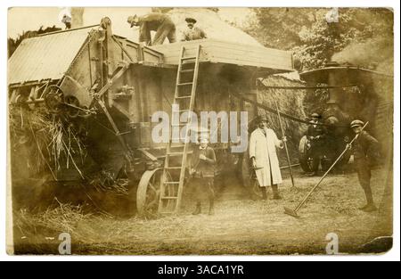 Carte postale originale du début des années 1900 représentant des agriculteurs utilisant une batteuse portative (remplacée plus tard par une moissonneuse-batteuse) alimentée par un moteur de traction à vapeur pour battre le blé sur une ferme au moment de la récolte. Mécanisation de l'agriculture. Gros fourrage derrière la batteuse. À moins qu'il ne s'agisse d'une grande ferme, cette batteuse a probablement été amenée sur le site et exploitée par des contacteurs. La plupart des entrepreneurs ont envoyé deux hommes avec chaque ensemble de battage, un pour s'occuper du moteur et l'autre pour alimenter le batteur. Les fermiers et les neigbours payés ont également contribué à la récolte. Hertfordshire, Angleterre, Royaume-Uni, c.1910 Banque D'Images