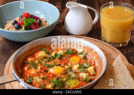 Petit déjeuner shakshuka et bol de granola avec un verre de jus d'orange sur une table en bois Banque D'Images