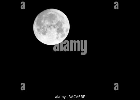 Une photographie minimaliste en noir et blanc de la pleine lune positionnée dans le coin supérieur gauche sur un fond complètement sombre, mettant en valeur les détails Banque D'Images