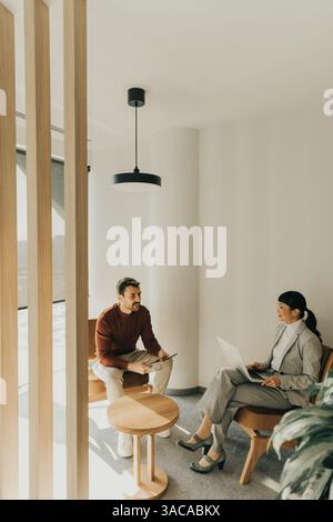 Deux professionnels s'engagent dans une discussion réfléchie dans un cadre de bureau élégant, échangeant des idées tout en étant confortablement assis dans des chaises contemporaines. Banque D'Images