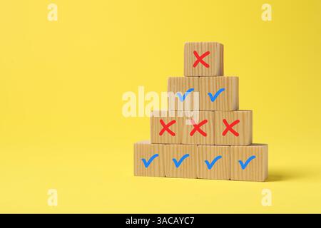 Approuver ou rejeter. Pyramide de cubes en bois avec des marques de contrôle et de croix sur fond jaune Banque D'Images