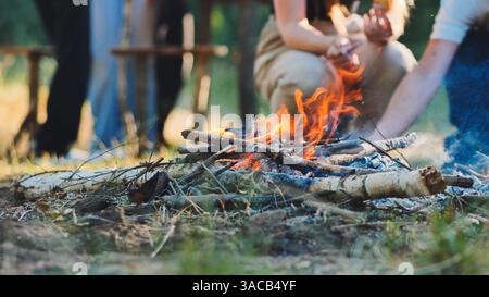 Feu de joie brûlant brillamment avec des amis debout autour de profiter de la chaleur et de la camaraderie dans la nature Banque D'Images