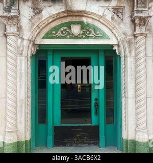 Une porte vert vif encadrée par des colonnes de pierre ornées et un fronton arqué avec des volutes décoratives et un motif bouclier. Banque D'Images