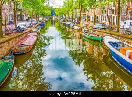 Amsterdam, pays-Bas. Vue panoramique sur les péniches, les bateaux à moteur et les voiliers bordant un canal un jour d'été. Banque D'Images