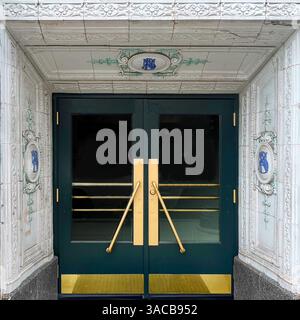 Portes élégantes avec poignées dorées et panneaux vert sarcelle, encadrées par des colonnes en terre cuite blanche ornée de monogrammes bleus dans un Chicago historique. Banque D'Images