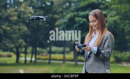 Femme d'affaires exploitant un drone avec télécommande dans le parc vert, profitant de la technologie innovante et de l'exploration aérienne Banque D'Images