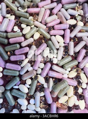 De nombreux compléments alimentaires de couleurs et de formes variées se trouvent dispersés sur une surface, y compris des capsules, des gels mous et des comprimés. L'assortiment reflec Banque D'Images