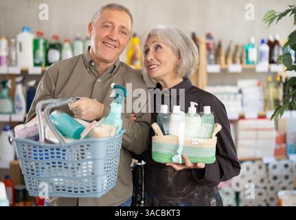 Couple mature avec panier complet choisissant des articles ménagers dans le supermarché Banque D'Images