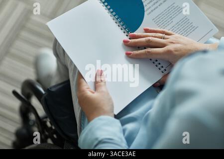 Gros plan de la jeune femme en fauteuil roulant lisant le livret d'entreprise tout en assistant à la conférence d'affaires sur le leadership, espace de copie Banque D'Images
