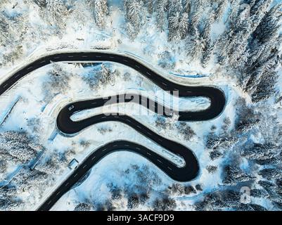 Voiture voyageant sur les virages en épingle à cheveux d'une route de montagne enneigée Banque D'Images