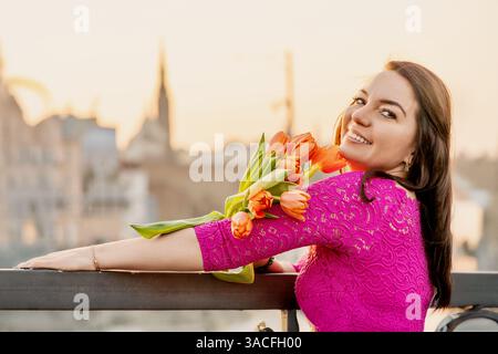 Femme souriant avec des tulipes dans une robe rose au coucher du soleil Banque D'Images