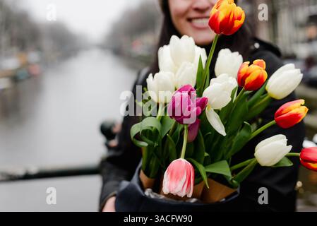 Femme souriante tenant un bouquet de tulipes avec Amsterdam canal en arrière-plan Banque D'Images