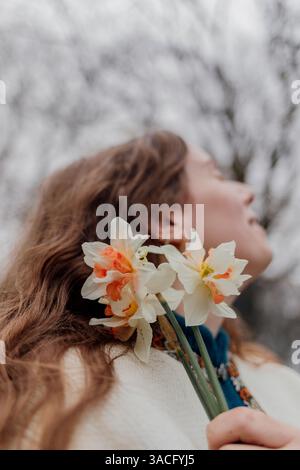 Femme tenant des jonquilles tout en regardant vers le haut dans un moment serein Banque D'Images