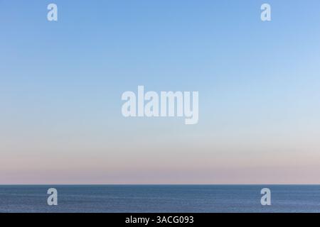 Paysage marin tranquille avec une mer encore bleue qui s'étend à l'horizon sous un ciel calme et dégradé aux couleurs subtiles à l'aube Banque D'Images
