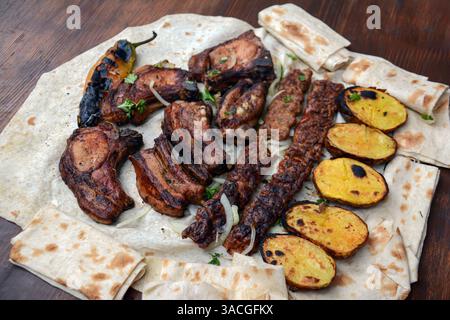 Barbecue avec viande grillée et shish kebab. Côtes d'agneau grillées, kebab, pommes de terre et pain pita sur planche de bois. Nourriture de restaurant, barbecue de porc, barbecue Banque D'Images