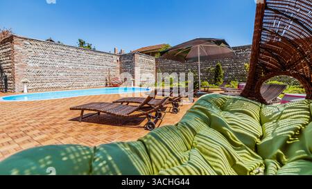 Luxueuse et accueillante retraite au bord de la piscine avec des chaises longues confortables sous un ciel bleu lumineux entouré d'éléments de jardin de bon goût et élégant Banque D'Images