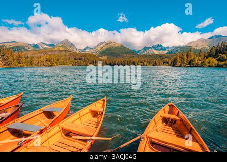 Bateau en bois de lac d'automne flottant sur l'eau calme, entouré de feuillage d'automne coloré, montagnes de ciel idylliques en arrière-plan, paysage naturel paisible Banque D'Images