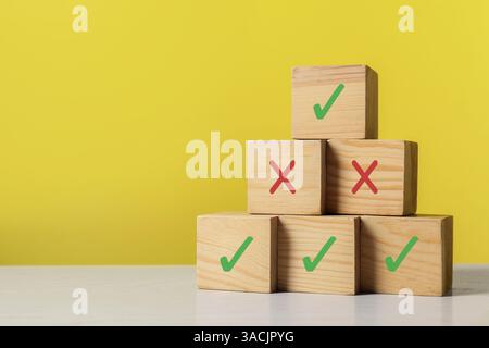 Approuver ou rejeter. Pyramide de cubes en bois avec des marques de contrôle et de croix sur fond jaune Banque D'Images