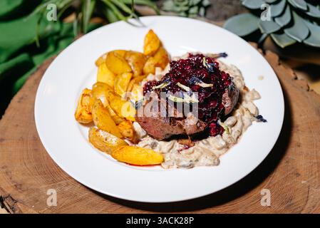 Bifteck gastronomique à la venaison nappé de sauce aux airelles, servi sur un ragoût de champignons crémeux et des quartiers de pommes de terre dorées rôties. Banque D'Images