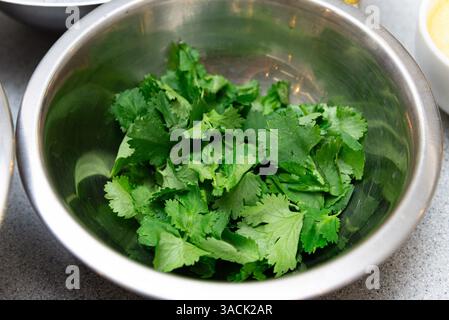 Bol rempli de feuilles de coriandre fraîchement cueillies, couramment utilisé comme garniture ou herbe dans diverses cuisines et recettes internationales. Banque D'Images