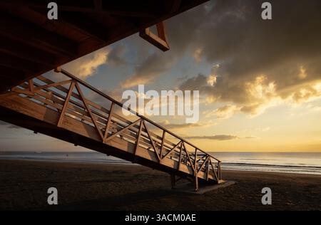 Un lever de soleil tranquille illumine une tour de sauveteurs en bois sur une plage de sable, avec un ciel nuageux créant une scène côtière pittoresque Banque D'Images