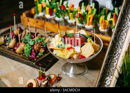 Gros plan d'un élégant buffet avec craquelins, fromage, fruits, trempettes, brochettes, et des tasses de légumes dans une configuration de restauration élégante. Banque D'Images