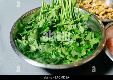 Herbes vertes comme le persil et la coriandre lavées dans un bol en métal, préparées pour être utilisées dans la cuisson ou la préparation de salades. Banque D'Images