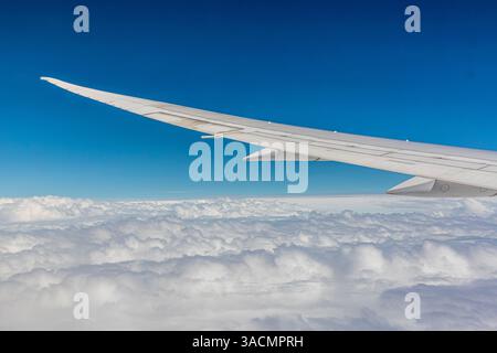Aile gauche (bâbord) d'un Boeing 787-9 posée contre un ciel bleu au-dessus de nuages blancs vus de la fenêtre passager quelque part près de Hong Kong Banque D'Images