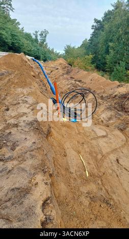 Construction de pipelines : le pipeline d'eau potable en plastique bleu est posé dans une tranchée profonde dans un sol sablonneux Banque D'Images